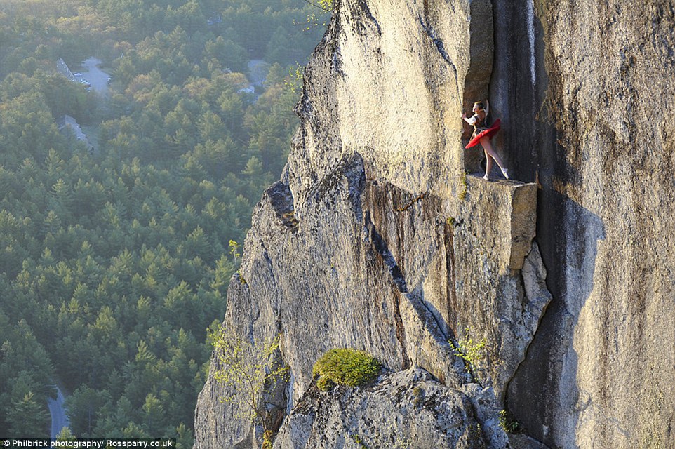 A ballerina in a red tutu practices her steps on a narrow cliff ledge while being photographed by Jay�